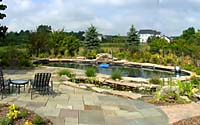 The product of the design process resulted in a formal, Pennsylvania bluestone patio for entertaining that leads to a free-form concrete swimming pool painted black and line with stone slabs to create a pond-like effect.